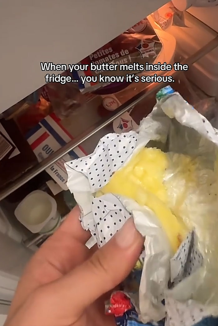 A hand holding a package of melted butter inside a refrigerator, showing Europeans trying to survive the heatwave.