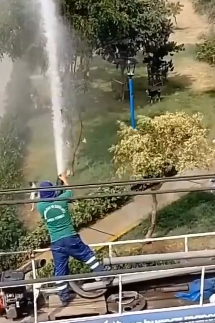A worker sprays water from a hose high into the air, trying to survive the heatwave.