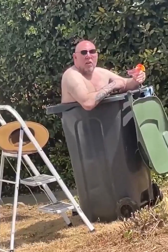 A shirtless European man in a large bin, holding a drink, trying to survive the heatwave.