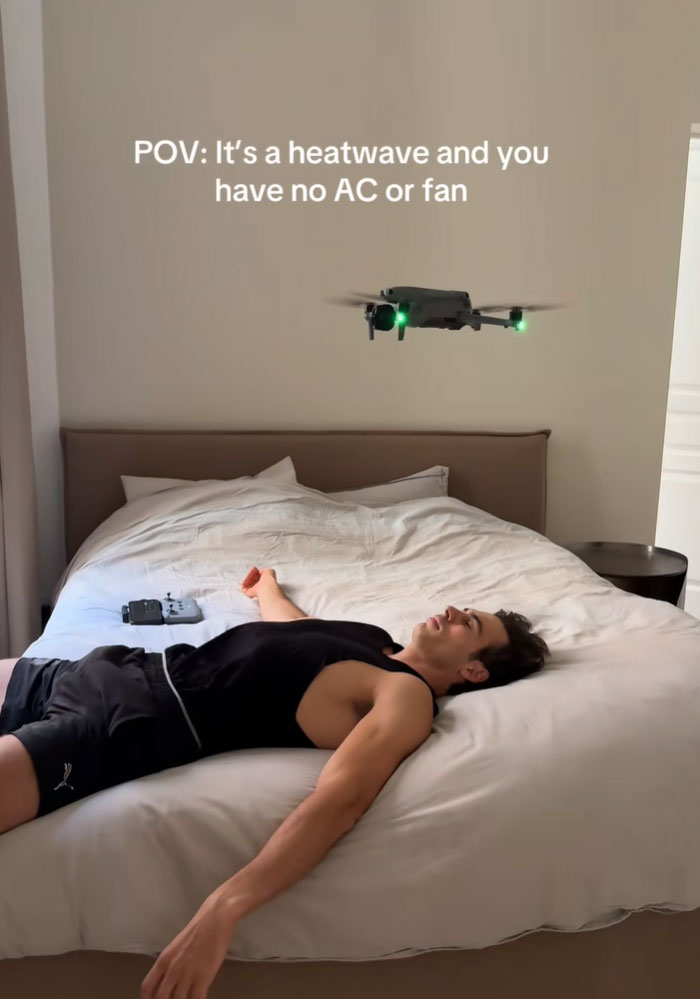 A man lying on a bed with a drone hovering above him for air during a heatwave.