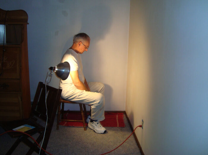 Man sitting alone in a corner lit by a lamp in a creepy, bare room