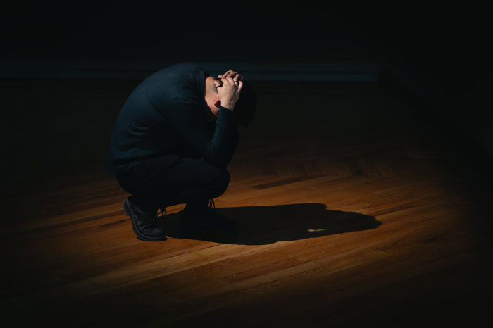 Man crouched in a spotlight struggling with a panic attack Man crouched in a spotlight struggling with a panic attack