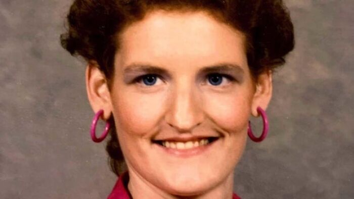 Woman with curly brown hair, blue eyes, and pink hoop earrings, part of an unsolved mystery.