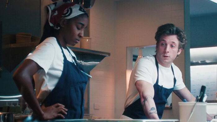 Carmy and Sydney from The Bear in a kitchen, discussing the chaotic final season and insufferable character.