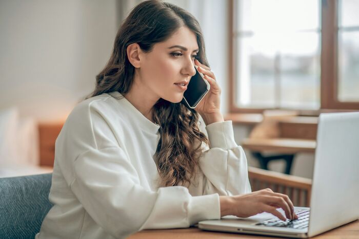 Woman talking on phone and typing on laptop representing work amid AI-caused great depression