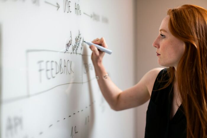 A woman writing feedback on a whiteboard, illustrating silly solutions to real problems.