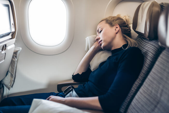 Woman resting on airplane seat beside window during generous travel experience