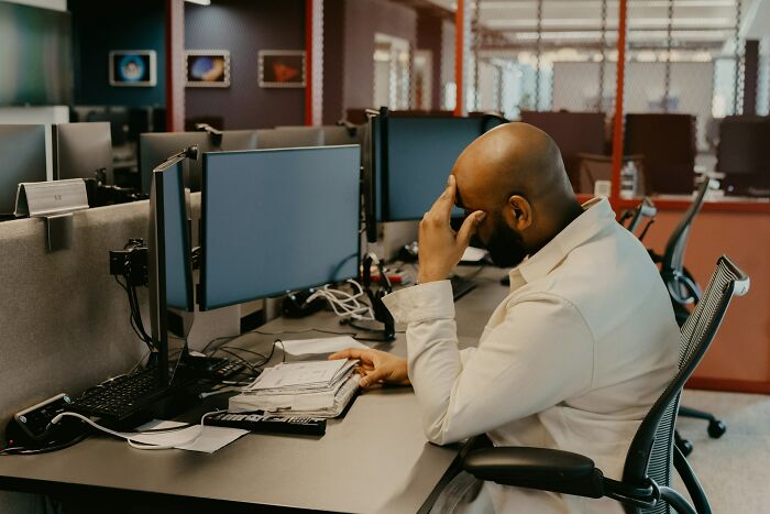 A man sitting at a desk, holding his head, showing signs of intense stress and burnout.
