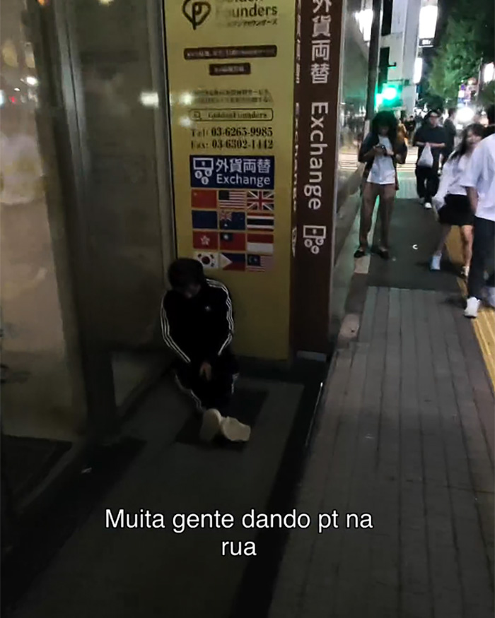 Image of the dark side of Japan, showing a person sitting on the ground next to a currency exchange sign, exposing a tourist's perspective.