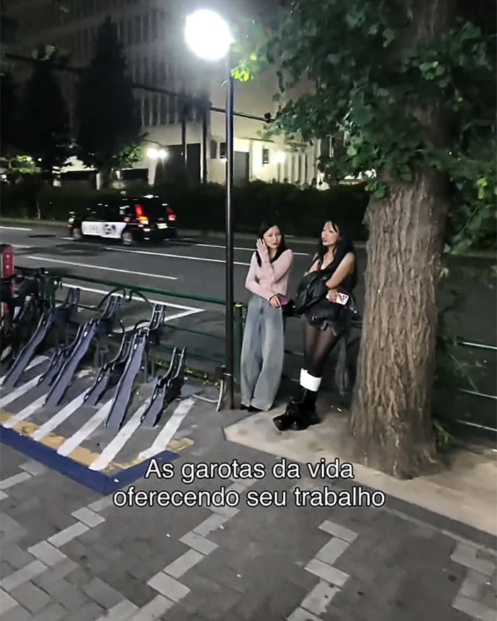 Two women standing by a tree on a street in Japan, exposing the dark side of local nightlife.