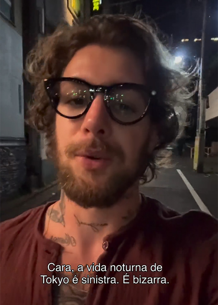 A tourist with glasses and a beard, in a dim street, exposing the dark side of Japan at night.