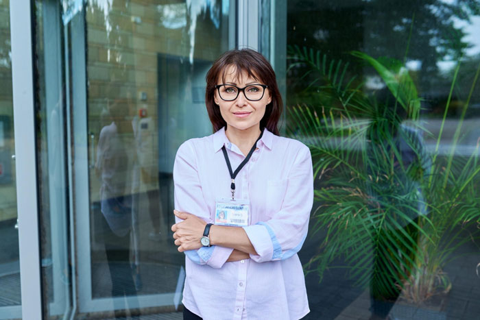 A woman wearing glasses and a pink shirt, standing with arms crossed, portraying the woman harassed by mommy dearest. A woman wearing glasses and a pink shirt, standing with arms crossed, portraying the woman harassed by mommy dearest.
