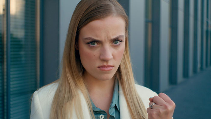 A woman with long blonde hair, wearing a white blazer, looks angrily at the camera, clenching her fist. Mommy dearest accuses woman of harassing. A woman with long blonde hair, wearing a white blazer, looks angrily at the camera, clenching her fist. Mommy dearest accuses woman of harassing.