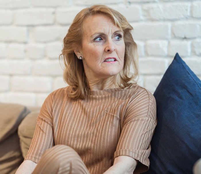 Worried older woman sitting on couch near blue pillow Worried older woman sitting on couch near blue pillow