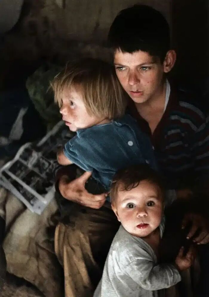 A historical photo of a boy holding two younger children, looking concerned, almost impossible to explain.