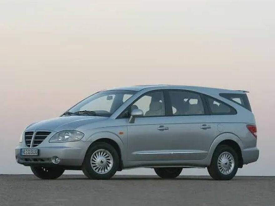 A silver SsangYong Rodius, an ugly car with an unusual design, parked outdoors.