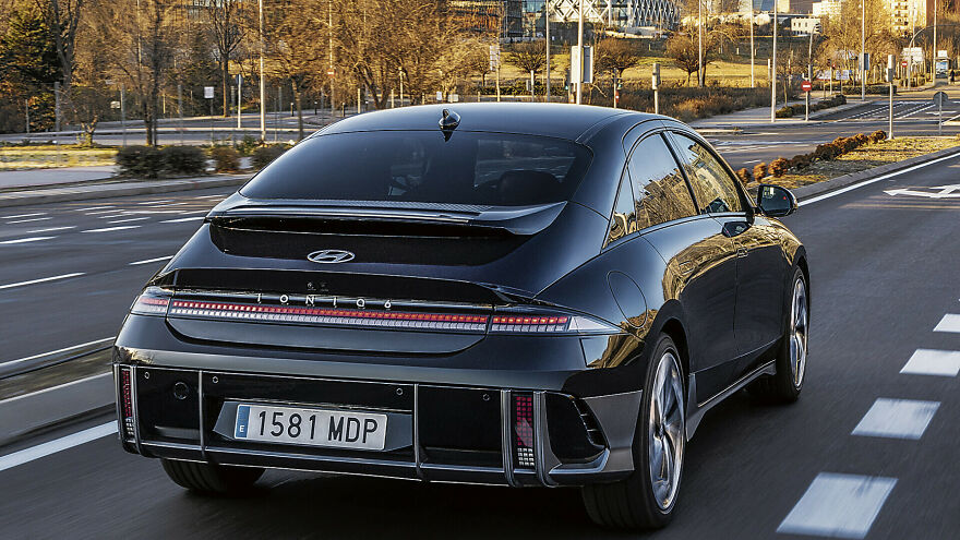A dark Hyundai Ioniq 6, an ugly legendary car, driving away on a multi-lane road.