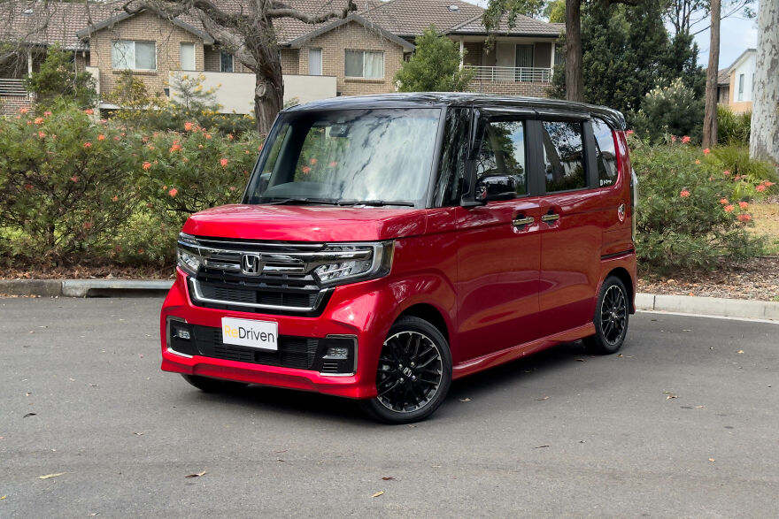 A red Honda N-Box, an ugly car that became legendary, parked on an asphalt driveway.