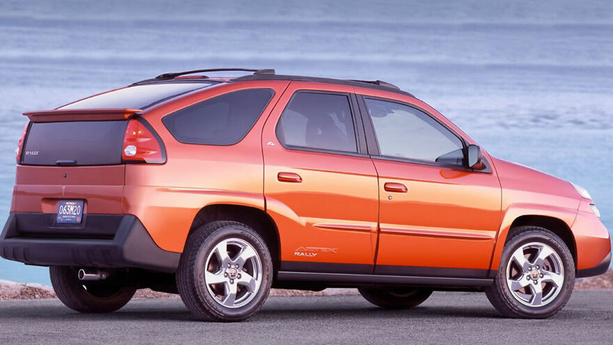 An orange Pontiac Aztek, an ugly car, parked outdoors with a body of water in the background. Legendary car.