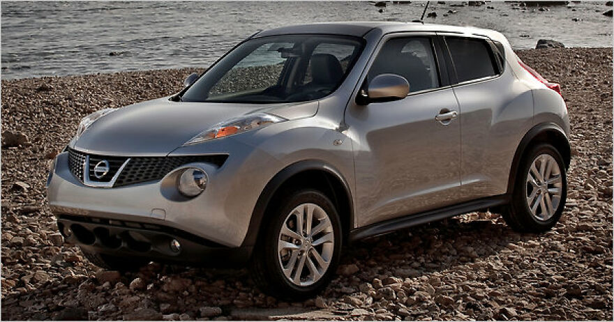 A silver Nissan Juke, an ugly car that became legendary, parked on a rocky beach.