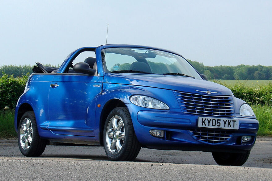 A blue Chrysler PT Cruiser convertible, an ugly car that became legendary, parked on a country road.