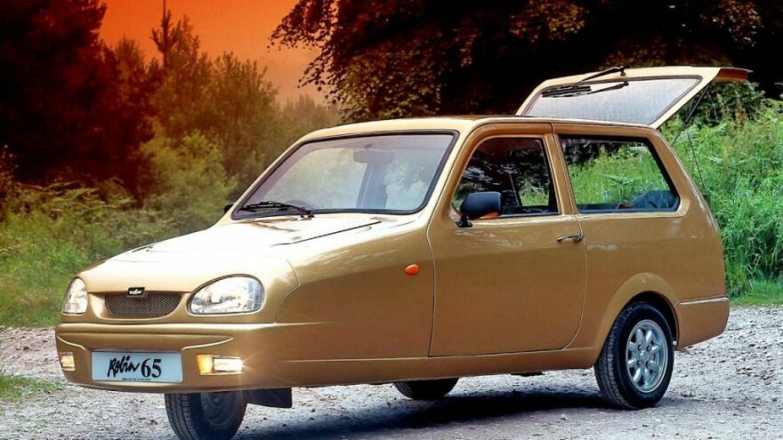 A gold Reliant Robin, one of the ugly cars, with its trunk open on a dirt road.