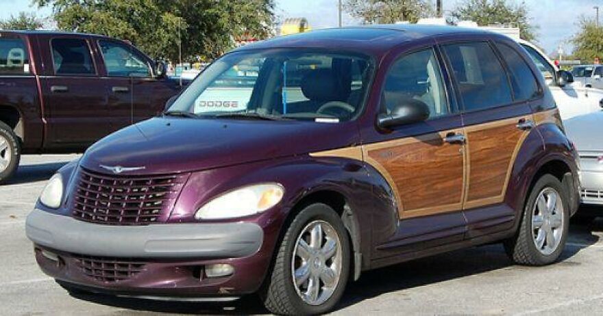 A purple Chrysler PT Cruiser with wood paneling, an ugly car, parked in a lot.