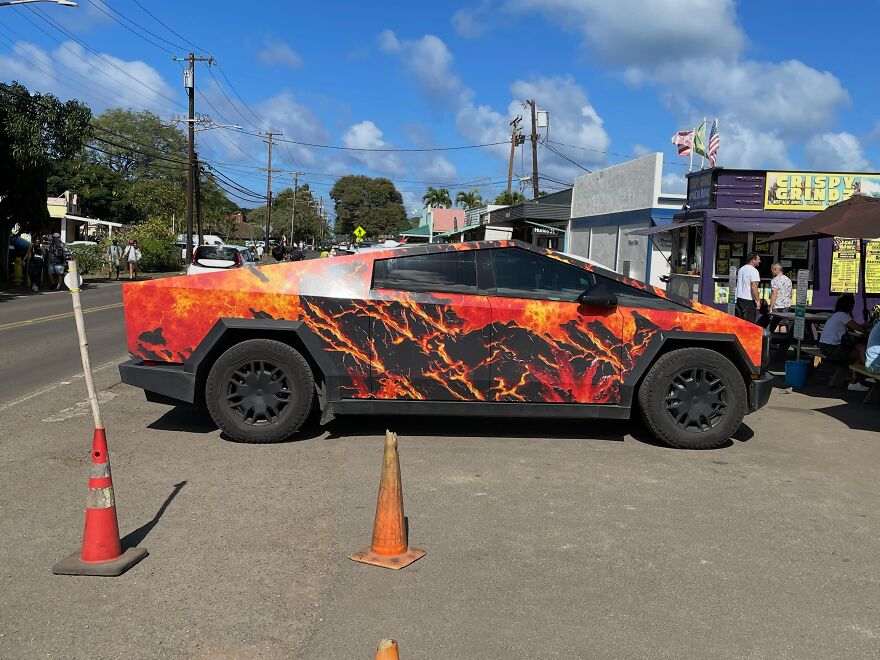 An ugly yet legendary car with a fire-patterned exterior, parked outdoors next to food stalls.