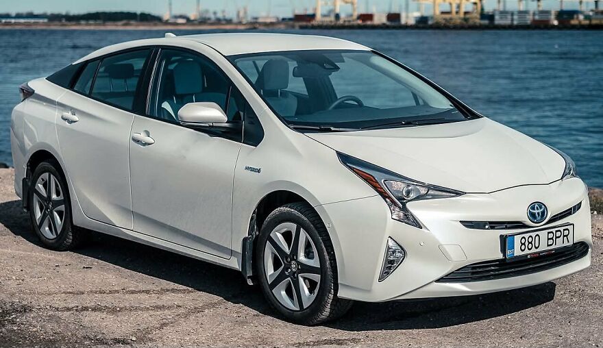 White Toyota Prius parked near a body of water under a clear sky, a legendary ugly car