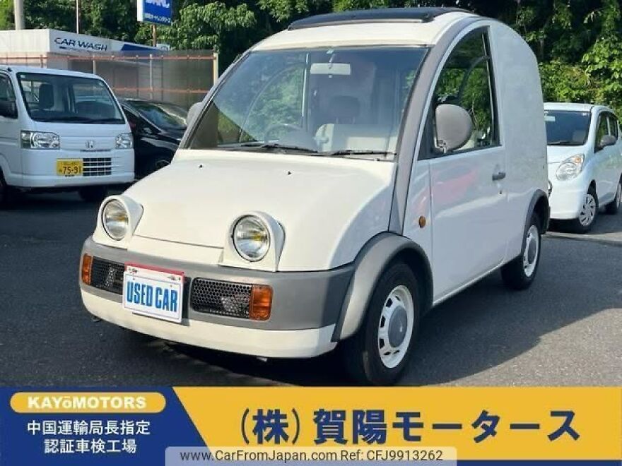 A white ugly car, a small van, with a USED CAR plate, parked in a lot, a legendary ugly car.