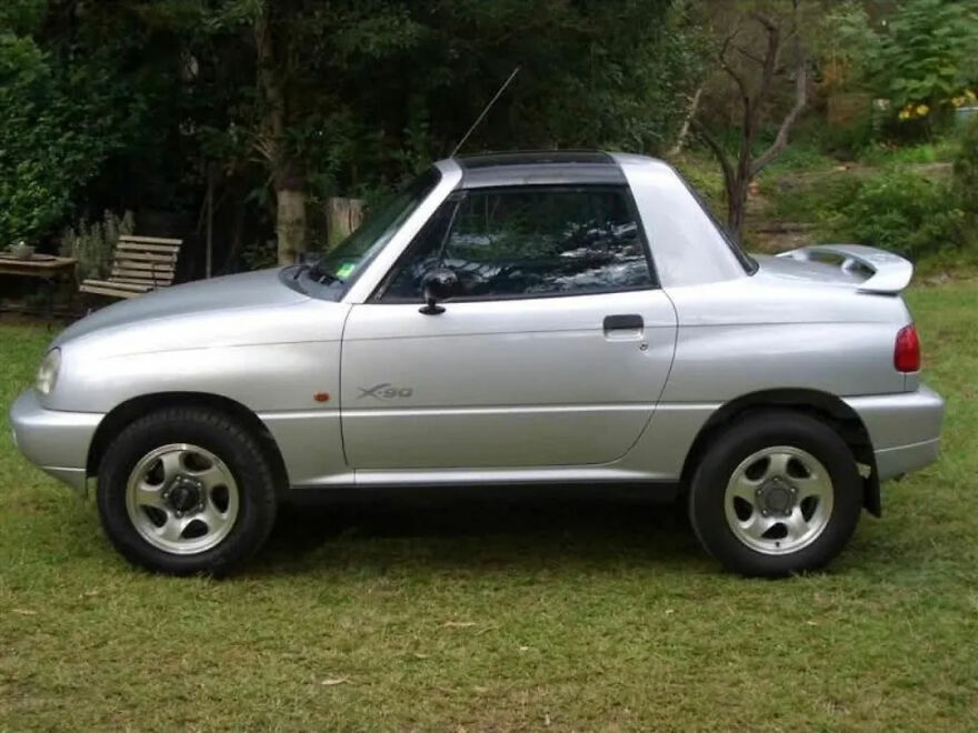 A silver ugly legendary car, a compact SUV, parked on green grass.