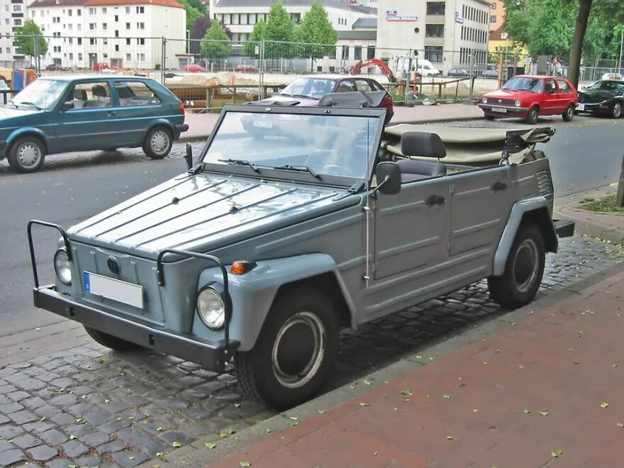 A grey Volkswagen Thing, an ugly car that somehow became legendary, parked on a cobblestone street in a city.