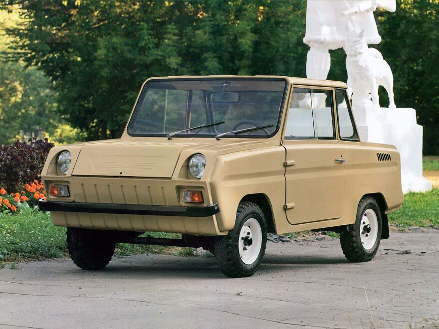 A vintage tan ZAZ-969M, an ugly car that became legendary, with a white statue in the background.