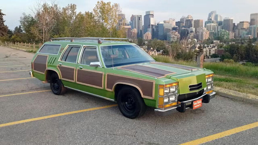 A green station wagon with wood paneling, one of the ugly cars that became legendary, with a city skyline.
