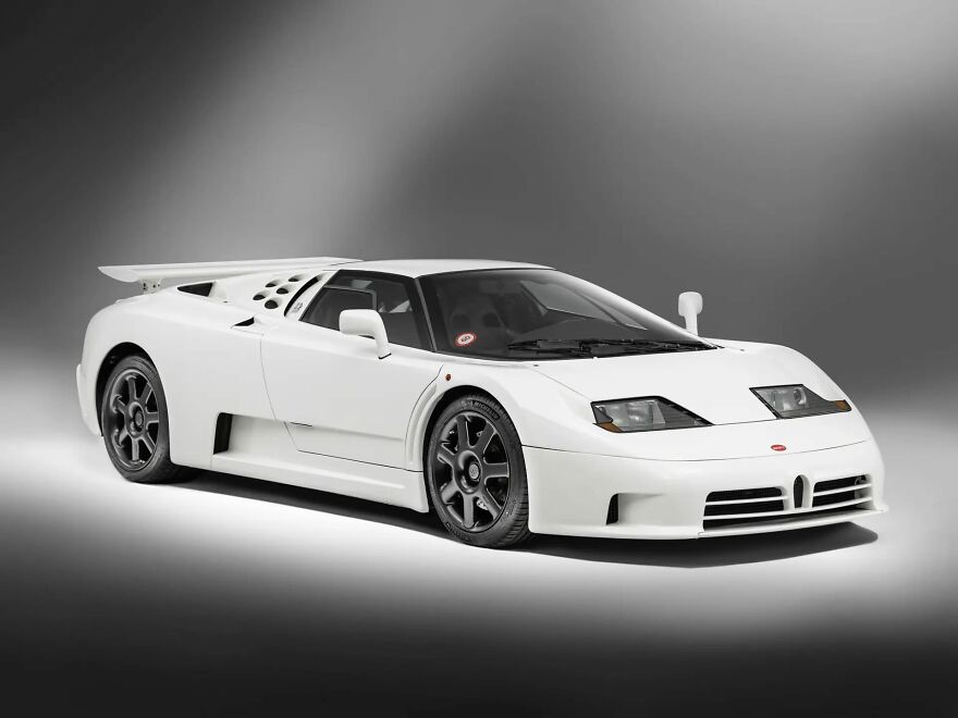 A white Bugatti EB110 GT, a legendary ugly car, shown in a studio setting.