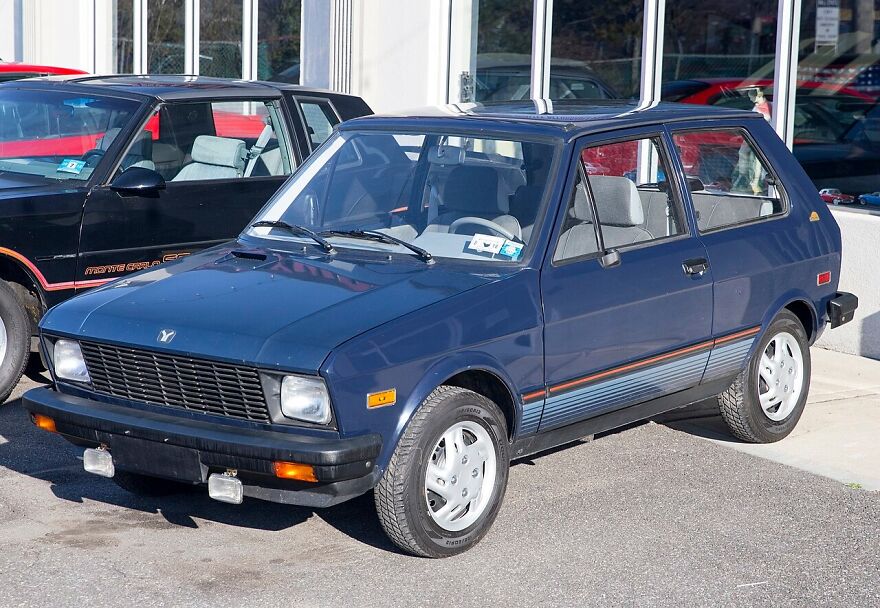 A navy blue Yugo hatchback, one of the ugly cars that became legendary, parked outdoors.
