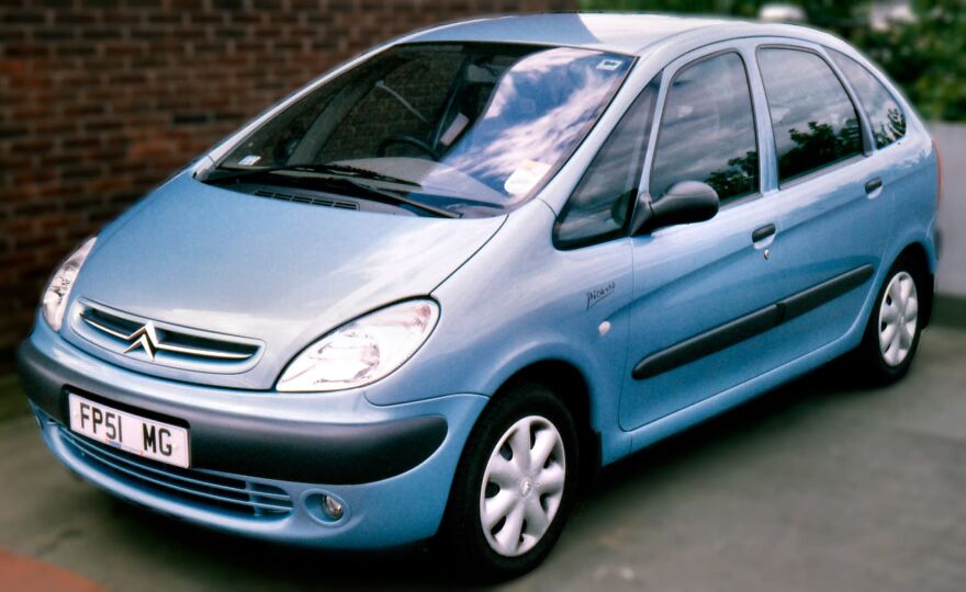A light blue Citroën Picasso, an example of ugly cars that are somehow legendary, parked on a paved surface.