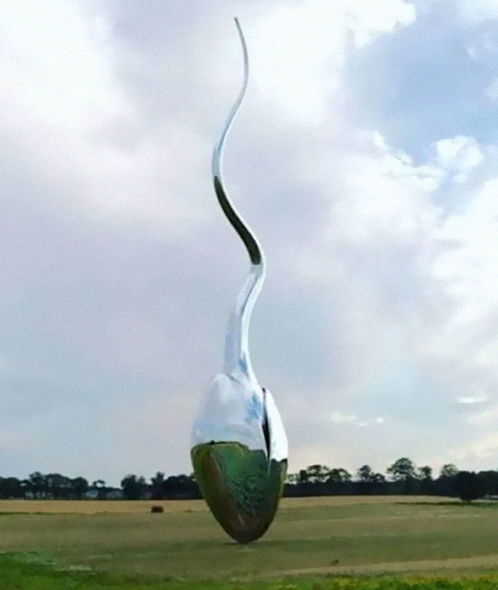 Tall twisted metallic spoon monument standing in a field under cloudy sky
