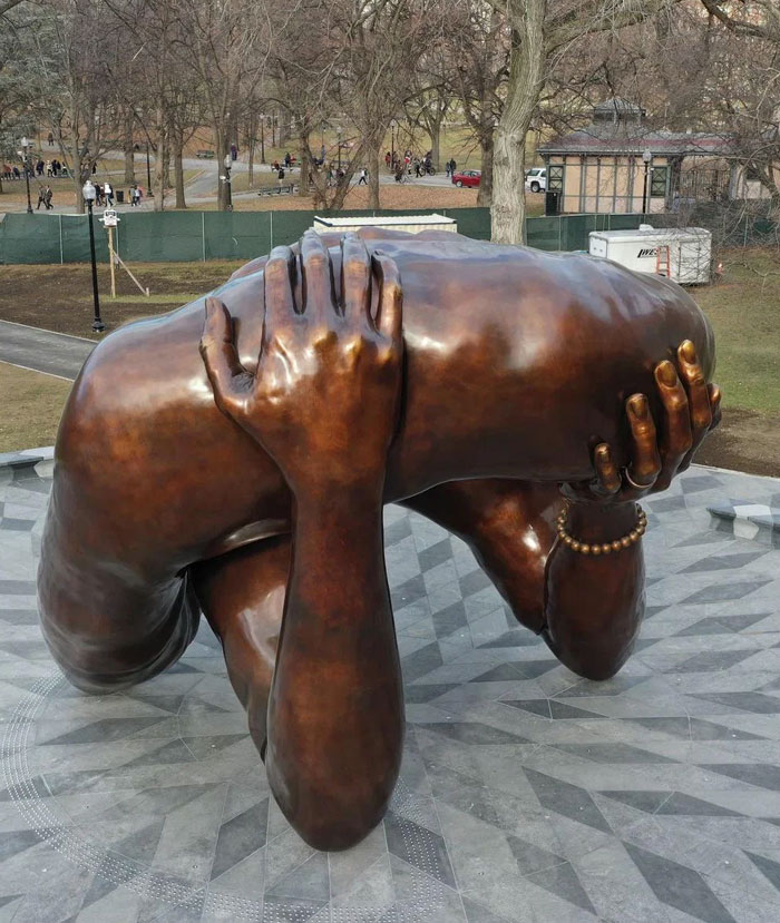 Bronze sculpture of a person holding their head in their hands in an outdoor park