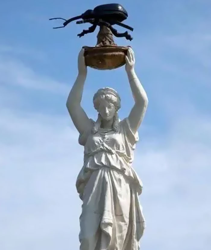 Classical statue holding a large beetle sculpture above its head against clear sky