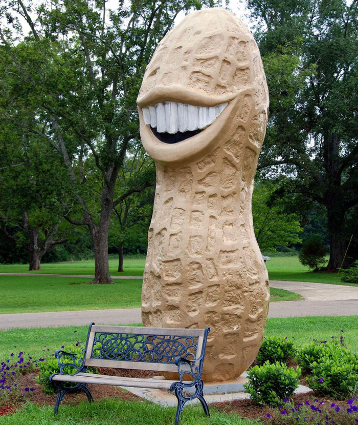 Ugly monument sculpture of a large smiling peanut with white teeth by a park bench