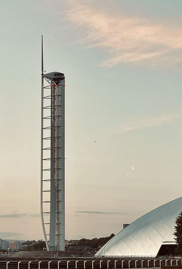 Tall modern architectural tower monument with curved structure at sunset