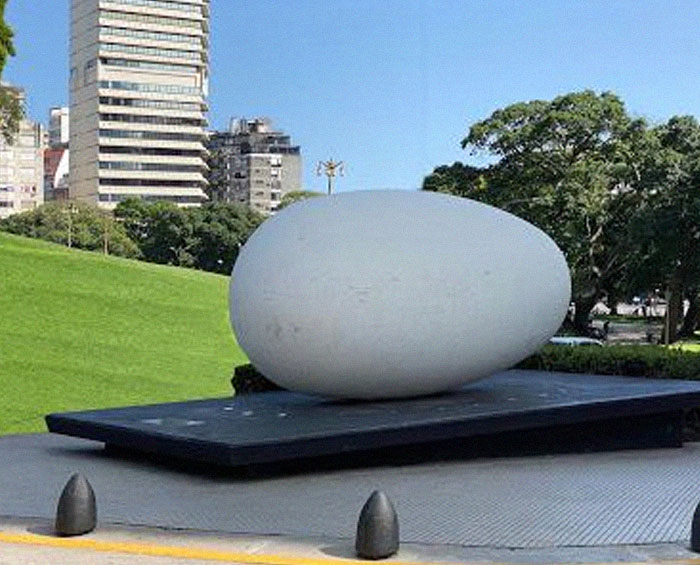 Minimalist large smooth egg-shaped monument on black platform outdoors