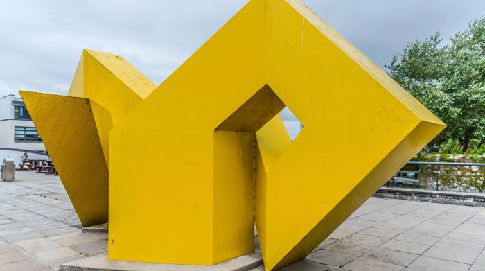 Large yellow abstract sculpture in urban square