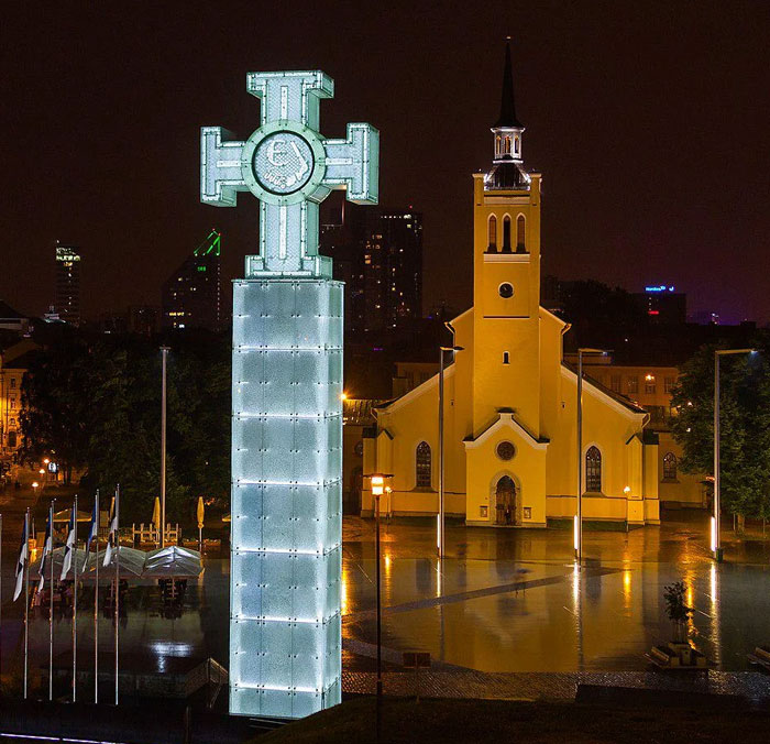 Illuminated cross-shaped monument near church at night