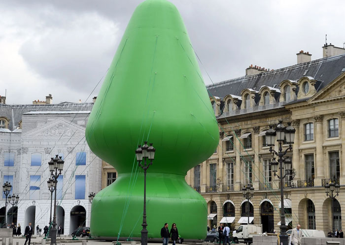Giant green inflatable sculpture resembling a b**t plug in city square