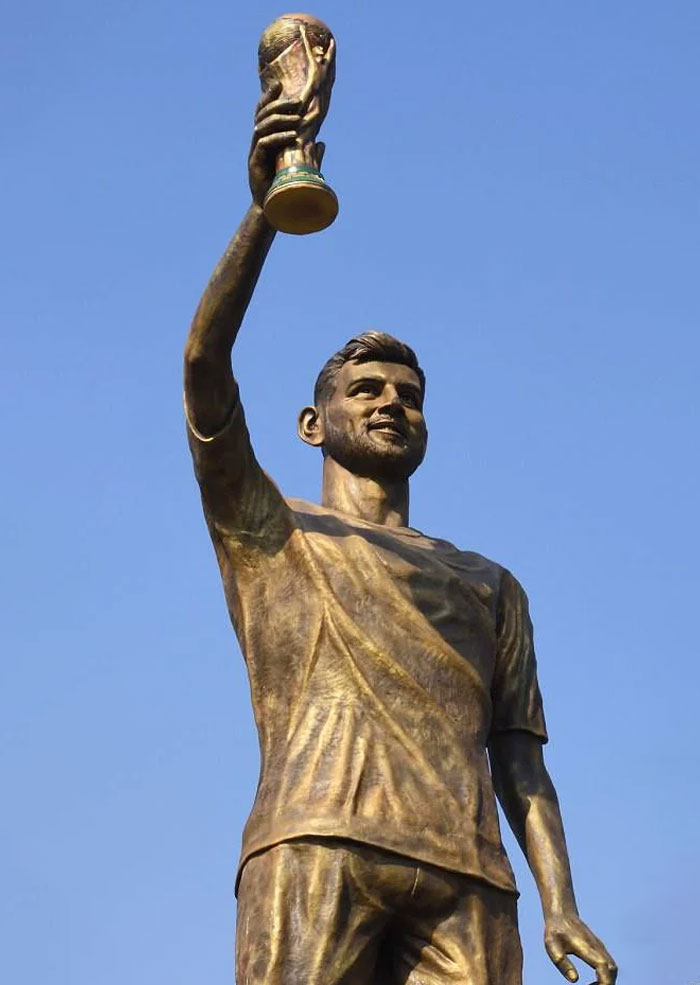 Bronze statue of man holding a trophy up high