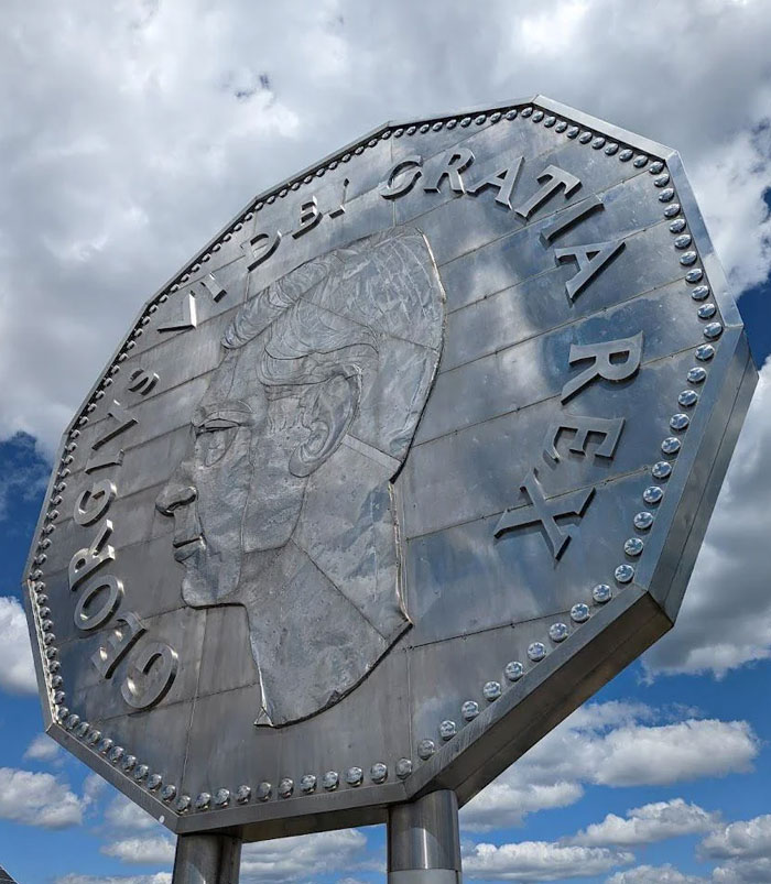Giant metal coin monument with profile of a man against cloudy sky