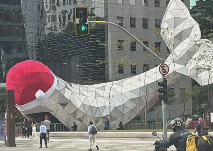 Large geometric whale monument wearing a Santa hat in urban setting
