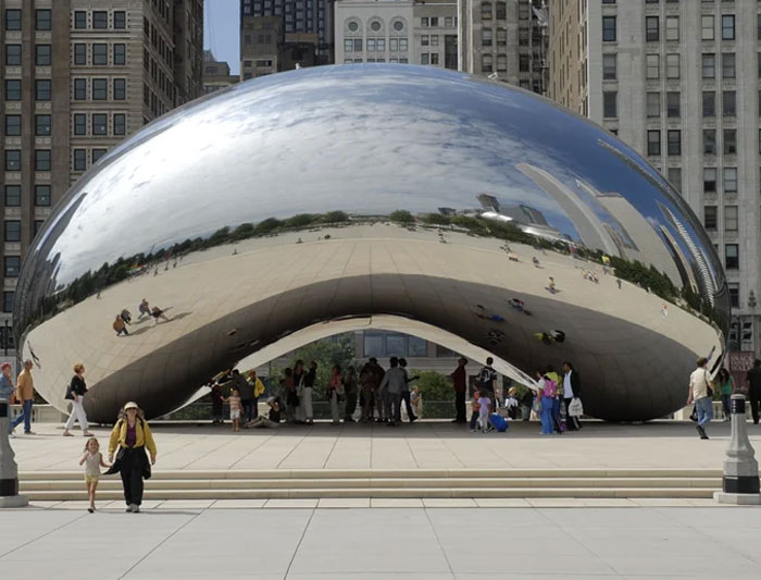 Reflective bean-shaped monument in city plaza with people around